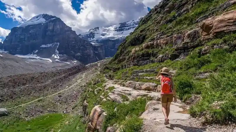 What Is the Best Backpack for Someone New to Hiking - top picture with a woman walking on a path in the mountains and carrying a pack.